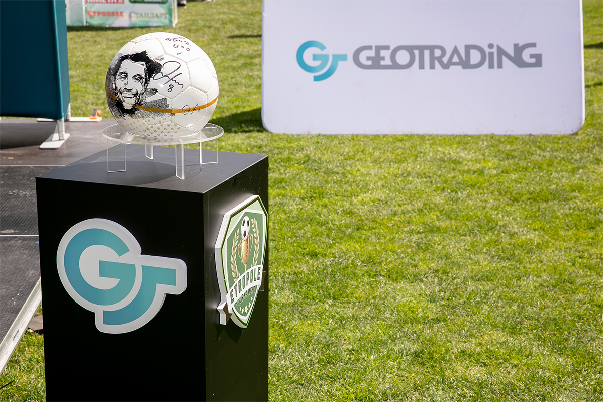 A soccer ball with Stoichkov's face, with a Geotrading banner in the background.